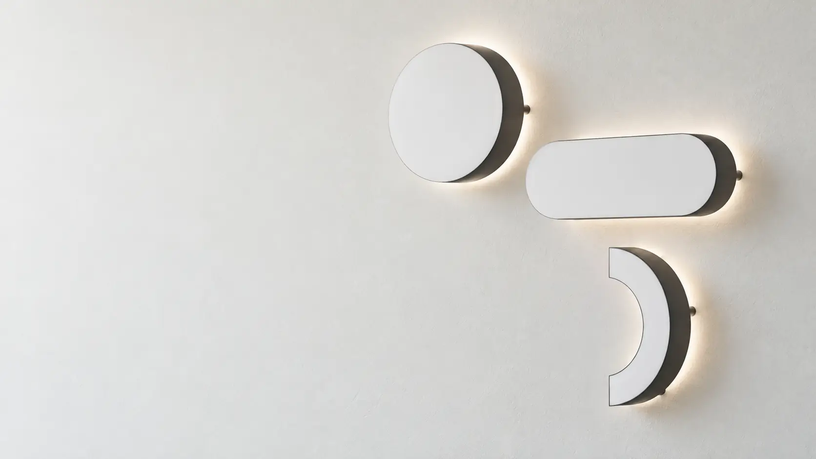 Three acrylic sign shapes with a soft white halo glow on a wall