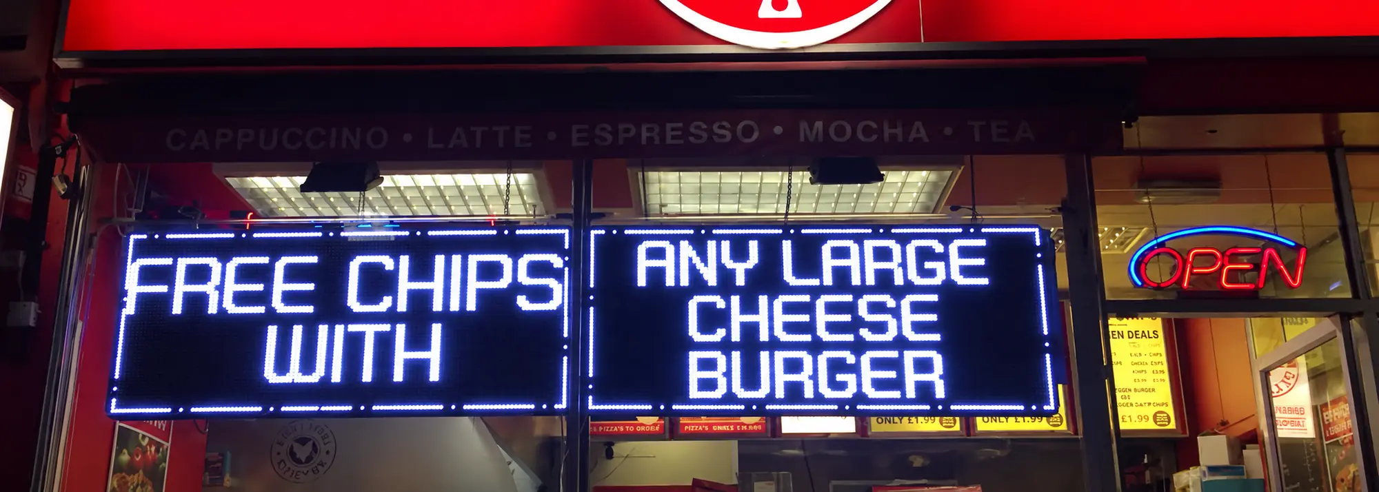 Two white LED message boards in a takeaway window reading "Free chips with any large cheese burger"