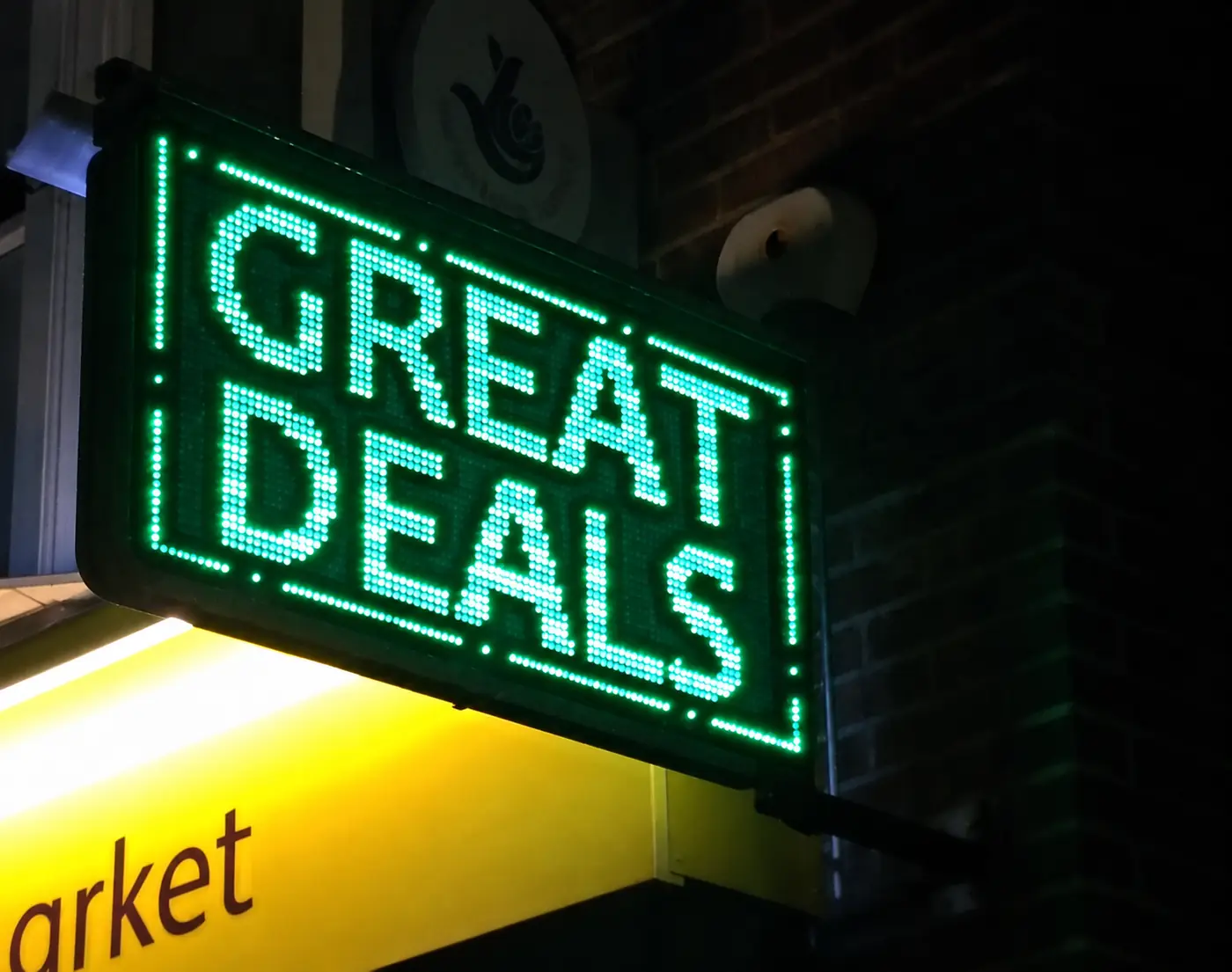 Green LED sign reading "Great deals" projecting from a shopfront at night