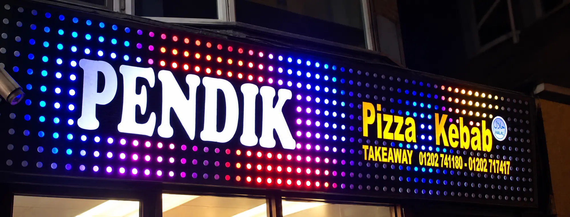 Night photo of a takeaway fascia covered in full-colour LED pixels, with the shop name in large white letters